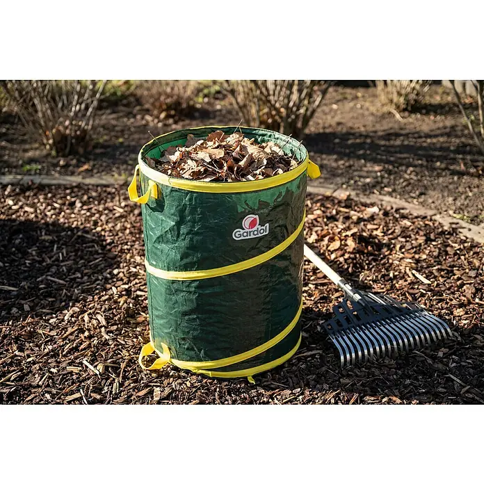 Gardol Pop-Up Gartenabfallsack - 120 l, Höhe: 60 cm, Durchmesser: 50 cm - Grüner aufklappbarer Gartenabfallsack, mit trockenen Blättern gefüllt, neben einem Rechen im Garten.