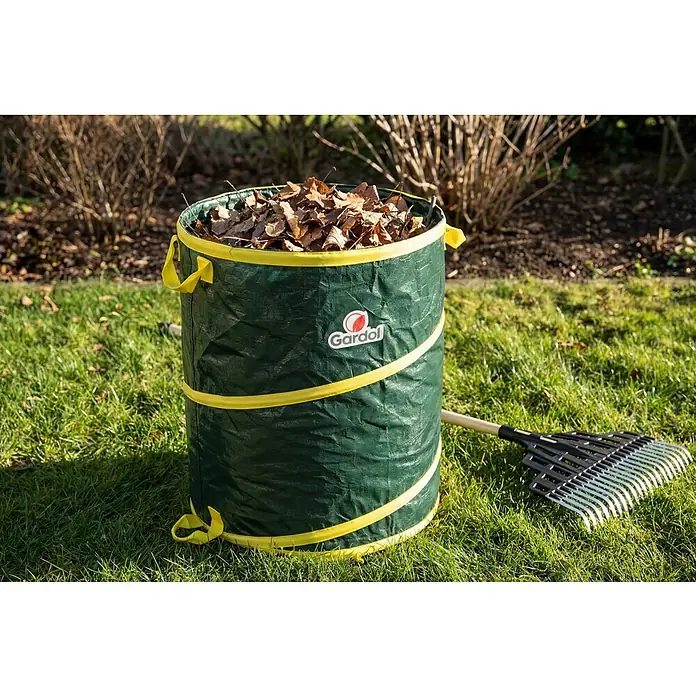 Gardol Pop-Up Gartenabfallsack - 120 l, Höhe: 60 cm, Durchmesser: 50 cm - Grüner Gartensack mit gelbem Rand, gefüllt mit trockenen Blättern, neben einer Harke.
