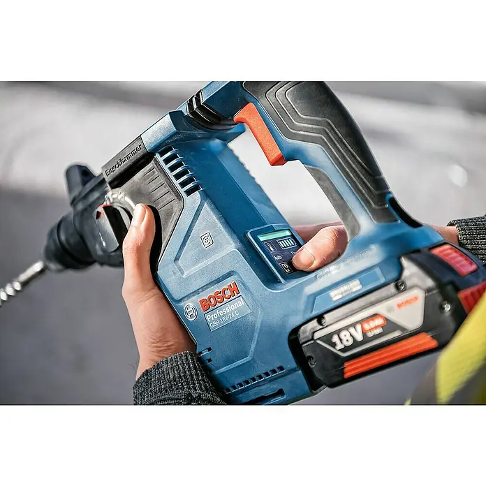 Bosch Professional AMPShare 18V Akku-Kombihammer GBH 18V-24 C - 18 V, 2 Akkus, 2,4 J - Nahaufnahme einer Person, die einen blauen Bosch Professional Akku-Bohrhammer hält, dessen Display und Akku sichtbar sind.