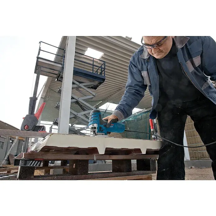 Bosch Professional Elektro-Stichsäge GST 150 CE - 500 /min - 3.100 /min - Mann in Schutzbrille benutzt eine blau-schwarze Bosch Oberfräse, um eine weiße Platte auf einer Baustelle zu bearbeiten.