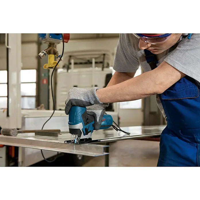 Bosch Professional Elektro-Stichsäge GST 90 E - 500 /min - 3.100 /min - Eine Person schneidet ein Metallprofil mit einer blau-schwarzen Bosch Stichsäge, Handschuhe und Schutzbrille tragend.