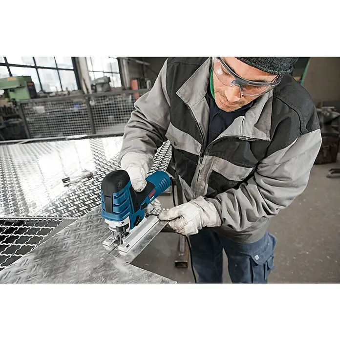 Bosch Professional Elektro-Stichsäge GST 150 CE - 500 /min - 3.100 /min - Mann mit Schutzbrille und Handschuhen benutzt eine blau-schwarze Bosch Stichsäge, um ein Metallblech zu schneiden.