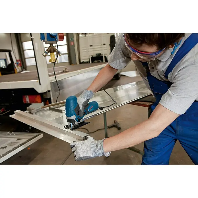 Bosch Professional Elektro-Stichsäge GST 90 E - 500 /min - 3.100 /min - Eine Person mit Schutzbrille und Handschuhen sägt mit einer blau-schwarzen Stichsäge ein silbernes Metallprofil.