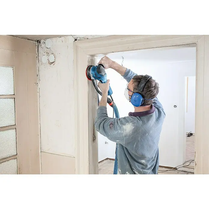 Bosch Professional Elektro-Exzenterschleifer GET 75-150 - 750 W, Durchmesser Schleifteller: 150 mm - Person schleift mit blauem Elektroschleifer und Absaugschlauch eine Wand ab.