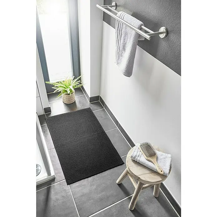 Badteppich Zottel - 50 x 80 cm, Schwarz, 100% Polyester - Dunkelgraue Noppen-Badematte auf Fliesenboden im Bad neben Dusche und Pflanze.