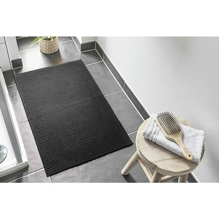 Badteppich Zottel - 50 x 80 cm, Schwarz, 100% Polyester - Dunkelgraue, strukturierte Badematte auf einem gefliesten Badezimmerboden neben einem Duschbereich.