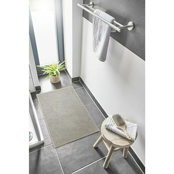 Badteppich Zottel - 60 x 100 cm, Grau, 100% Polyester - Hellgraue, strukturierte Badematte auf dunklem Fliesenboden im Badezimmer.
