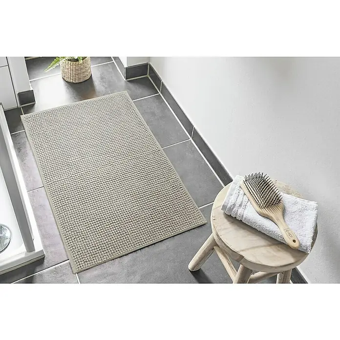 Badteppich Zottel - 60 x 100 cm, Grau, 100% Polyester - Hellgraue strukturierte Badematte auf dunklem Fliesenboden neben einer Dusche.