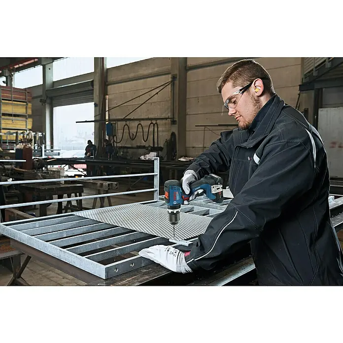 Bosch Professional AMPShare 18V Akku-Schlagbohrschrauber GSB 18V-65 - 18 V, 2 Akkus, 4 Ah, 63 Nm, 2 x 4 Ah Akku, L-BOXX 136 - Mann in Arbeitskleidung bohrt mit einem blau-schwarzen Bosch Professional Akku-Bohrschrauber in ein Metallgitter.