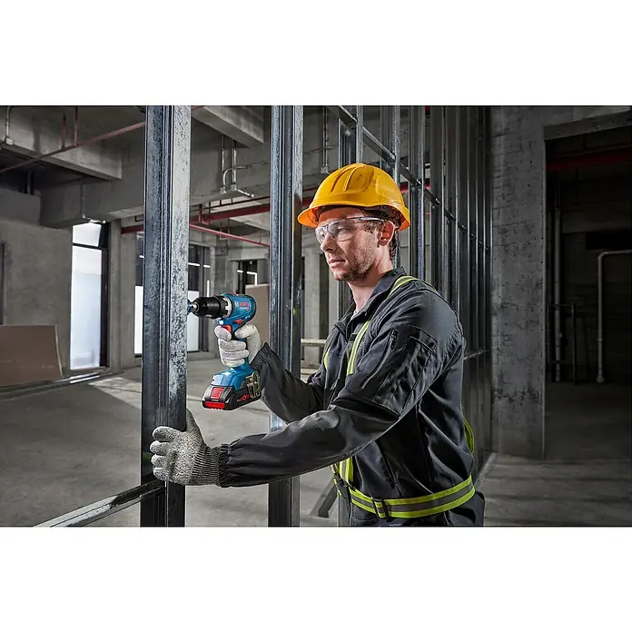Bosch Professional AMPShare 18V Akku-Bohrschrauber GSR 18V-65 - 18 V, 2 Akkus, 4 Ah, 76 Nm, 2 x 4 Ah Akku, mit L-BOXX-Koffer - Arbeiter mit blauem Bosch Akkuschrauber bohrt in Metallrahmen. Trägt Schutzhelm und Schutzbrille.