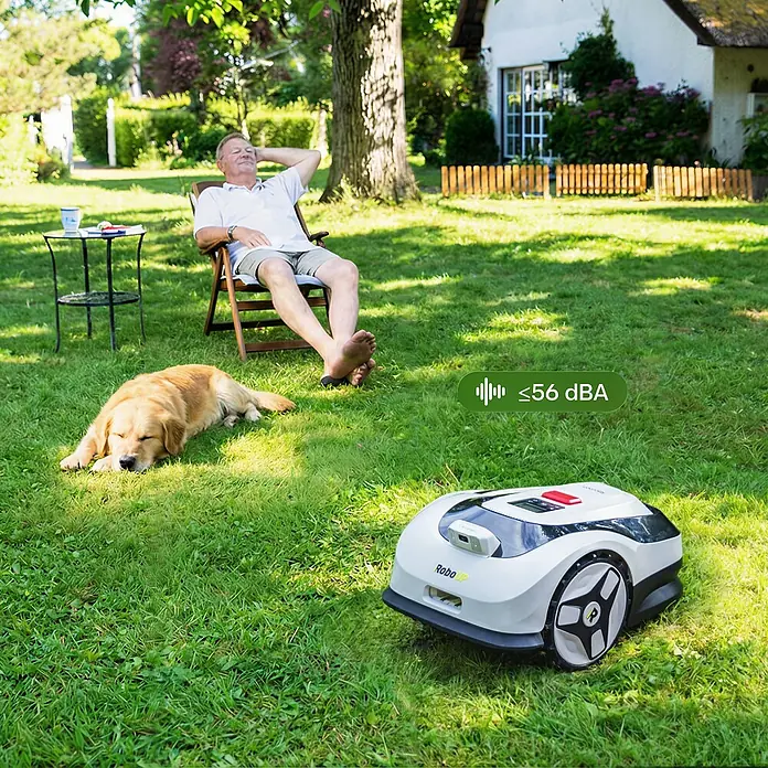 RoboUp Mähroboter Raccoon 2 SE - 600 m², Schnittbreite: 20 cm, Kamera-gestützte Navigation - Weiß-schwarzer Rasenroboter arbeitet leise im Garten. Ein Mann entspannt und ein Hund schläft in der Nähe.