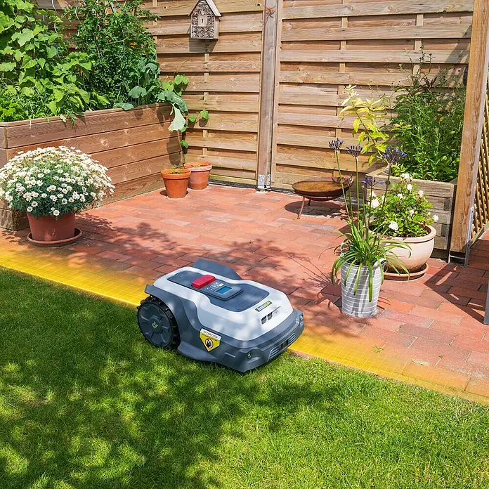 RoboUp Mähroboter T1200 - 1.500 m², Schnittbreite: 20 cm, Kamera-gestützte Navigation, RTK - Ein grau-weißer Mähroboter auf grünem Rasen neben einer Ziegelterrasse. Eine gelbe Linie zeigt die Begrenzung an.