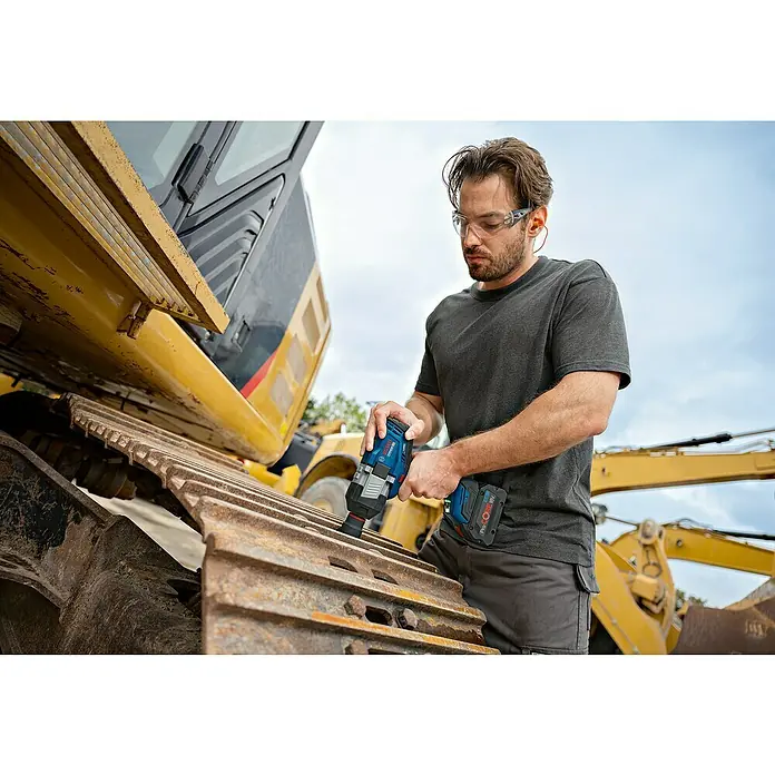 Bosch Professional AMPShare 18V Akku-Drehschlagschrauber GDS 18V-1600 HC - 18 V, Ohne Akku, 1.600 Nm, Ohne Akku, ohne Koffer - Mann in Schutzausrüstung verwendet blauen Bosch Akku-Schlagschrauber an rostiger Baggerschiene.