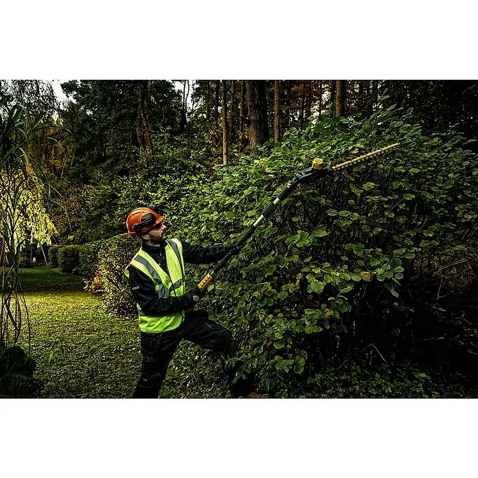 DeWalt XR 18V Teleskop-Heckenschere DCMPH566N-XJ - 18 V, Anzahl Akkus: Ohne Akku - Mann in Schutzkleidung schneidet eine große Hecke mit einer schwarz-gelben Teleskop-Heckenschere.