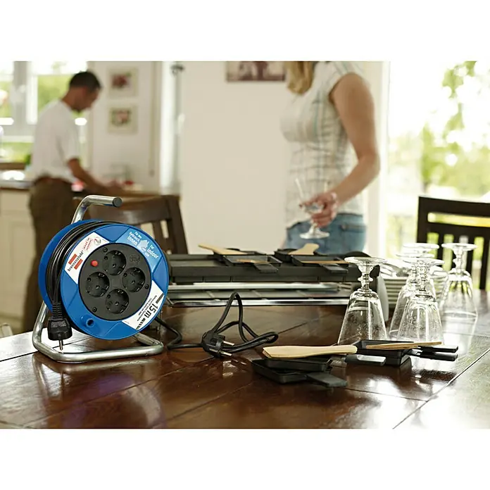 Brennenstuhl Kabeltrommel - Spezialkunststoff, 15 m, H05VV-F, IP20 - Eine blaue Brennenstuhl Kabeltrommel mit vier Steckdosen und ein Raclette-Grill-Set stehen auf einem Holztisch für ein geselliges Abendessen.