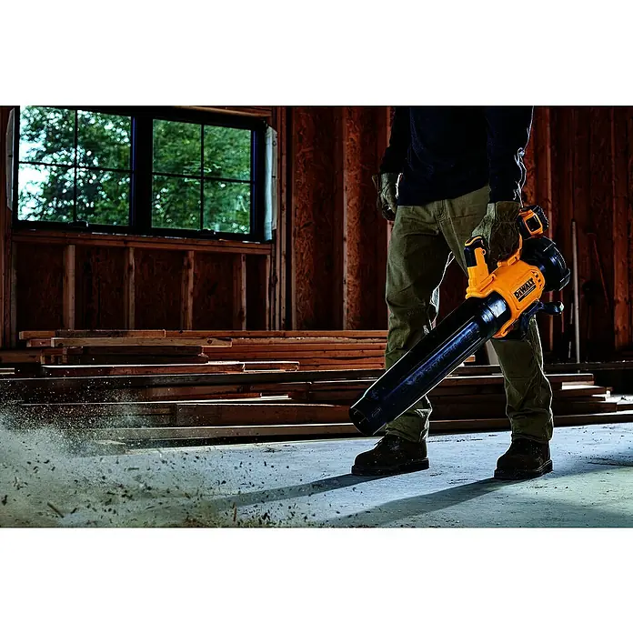 DeWalt XR 18V Akku-Gebläse DCMBL562N-XJ - 18 V, Ohne Akku, Blasgeschwindigkeit: 0 km/h - 200 km/h - Person in Arbeitskleidung benutzt einen gelb-schwarzen DeWalt Laubbläser, um Schmutz von einem Boden in einer Holzbaustelle zu entfernen.