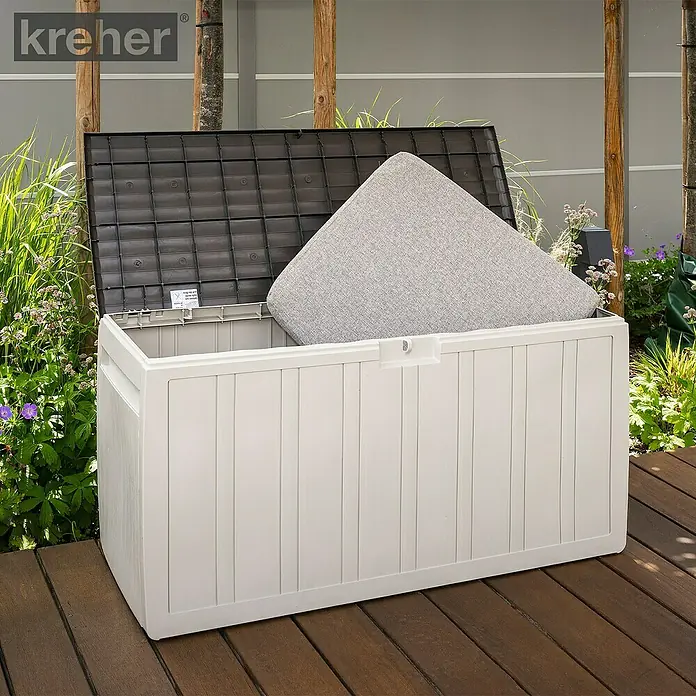 Kissenbox - 45,5 x 117 x 57,5 cm, Kunststoff, Beige - Beigefarbene Outdoor-Kissenbox mit offenem dunkelbraunem Deckel, einem hellgrauen Kissen auf Holzterrasse.