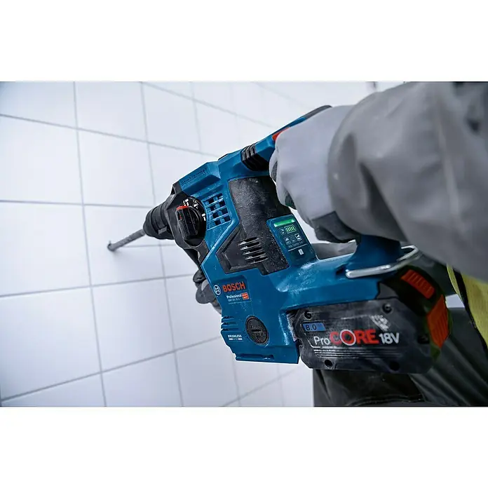 Bosch Professional AMPShare 18V Akku-Kombihammer Pro Heavy Duty GBH 18V-28 C - 18 V, Ohne Akku, 3,3 J, Mit L-BOXX - Blauer und schwarzer Bosch Bohrhammer mit ProCORE 18V Akku bohrt in eine weiße Fliesenwand, gehalten von behandschuhten Händen.