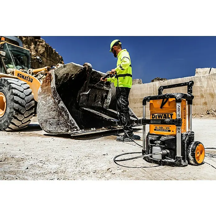 DeWalt XR 18V Akku-Hochdruckreiniger DCMPW1600N-XJ - 18 V, Ohne Akku - Gelb-schwarzer DeWalt Hochdruckreiniger reinigt einen Komatsu Baggerlöffel, bedient von einem Arbeiter auf der Baustelle.