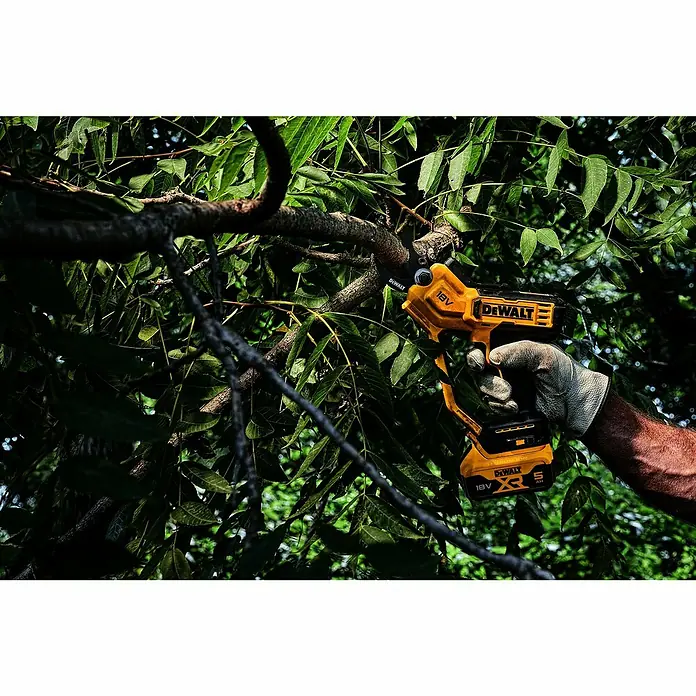 DeWalt XR 18V Akku-Astschere DCMPP568N-XJ - Max. Aststärke: 38 mm - Eine behandschuhte Hand schneidet mit einer gelb-schwarzen DeWalt Akku-Astschere einen Ast in einem belaubten Baum.