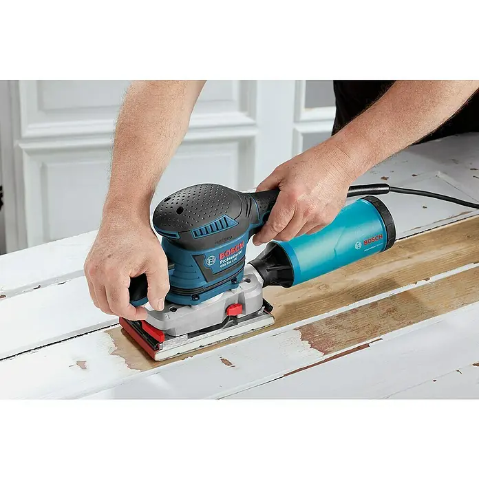 Bosch Professional Elektro-Schwingschleifer GSS 230 AVE - 300 W - Eine Person schleift ein Holzbrett mit einem blau-schwarzen Bosch Schwingschleifer, an dem ein türkiser Staubsammelbehälter befestigt ist.
