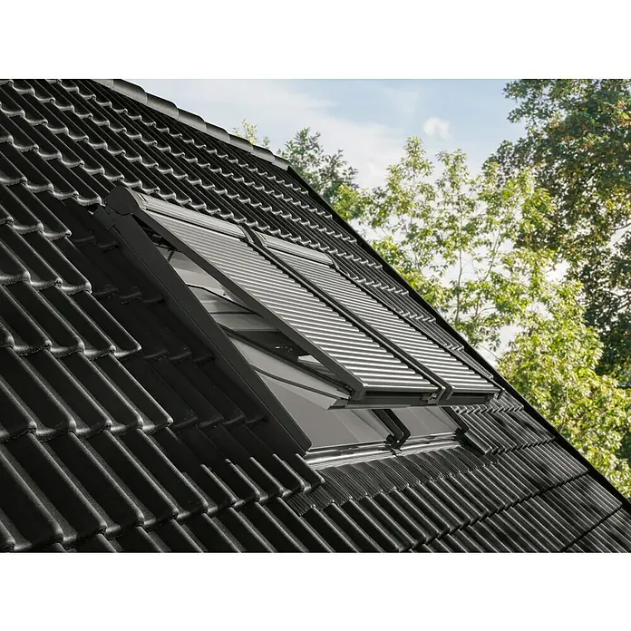 Velux Dachfenster-Rollladen Elektro SML CK06 0000K - Passend für Fenstergröße: CK06, C06, Passend für Fenstertyp: GGL, GGU, GPL, GPU, GHL, GHU, GZL, GLL, GLU, VU und VKU - Zwei dunkle Dachfenster mit teilweise ausgefahrenen silbernen Außenrollläden auf einem schwarzen Ziegeldach.