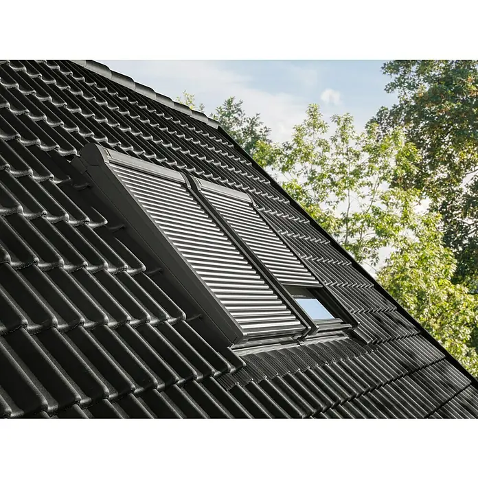 Velux Dachfenster-Rollladen Elektro SML CK06 0000K - Passend für Fenstergröße: CK06, C06, Passend für Fenstertyp: GGL, GGU, GPL, GPU, GHL, GHU, GZL, GLL, GLU, VU und VKU - Zwei dunkle Außenrollläden auf Dachfenstern eines schwarzen Ziegeldachs installiert. Ein Rollladen ist teilweise geöffnet.