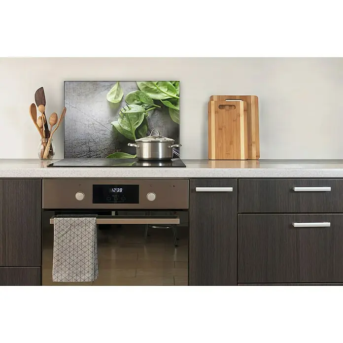 CUCINE Küchenrückwand - Basil on Fork, 60 x 40 cm, Stärke: 6 mm, Einscheibensicherheitsglas (ESG) - Küchenstillleben mit Kochutensilien, Schneidebrettern und einem Topf auf dem Herd, vor einer Küchenrückwand mit Spinatmotiv.