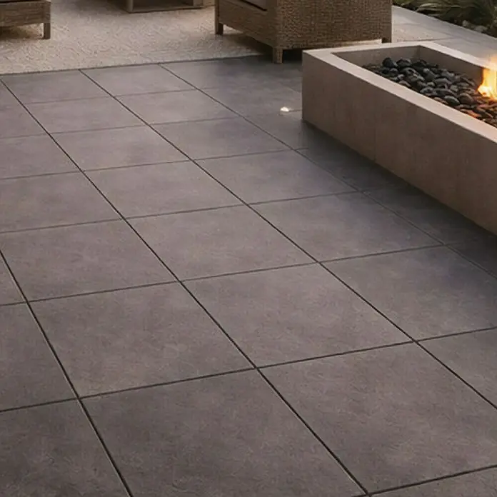 Terrassenfliese Urban Pro - 60 x 60 x 2 cm, Anthrazit, Matt - Große dunkelgraue quadratische Terrassenplatten als Außenboden neben einer Feuerstelle.