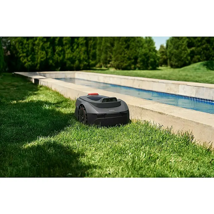 Mova Mähroboter Viax 300 - 300 m², Schnittbreite: 20 cm, Kamera-gestützte Navigation - Ein schlanker grauer Rasenroboter mit schwarzen und roten Akzenten, Carbonfaser-Textur, auf Rasen neben einem Wasserkanal.