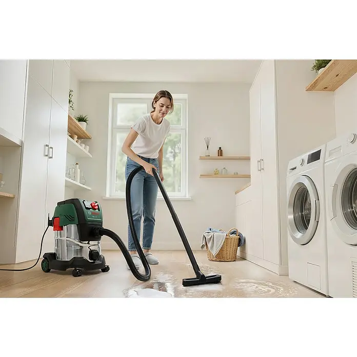 Bosch Elektro-Nass- & Trockensauger PAS 20-220P - 1.350 W, Behältervolumen: 20 l - Eine Frau saugt mit einem grün-silbernen Bosch Nass-Trockensauger eine Flüssigkeit von einem Holzboden in einem Waschraum auf.