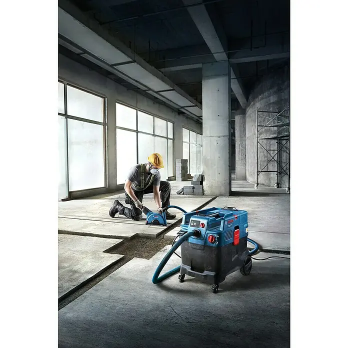 Bosch Professional Elektro-Nass- & Trockensauger PRO GAS 400 A - 1.200 W, Behältervolumen: 40 l, Vollautomatisch - Ein Arbeiter nutzt eine blaue Bosch Mauernutfräse, verbunden mit einem blau-schwarzen Bosch Sauger, und schneidet Nuten in Beton.