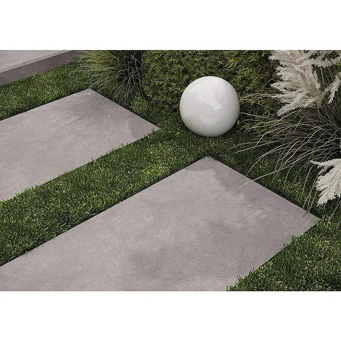 Cersanit Terrassenfliese Metropolis - 59,3 x 119,3 x 2 cm, Grey, Matt - Graue Betonplatten in grünem Gras, mit einer weißen Kugel-Gartenleuchte und Zierpflanzen.