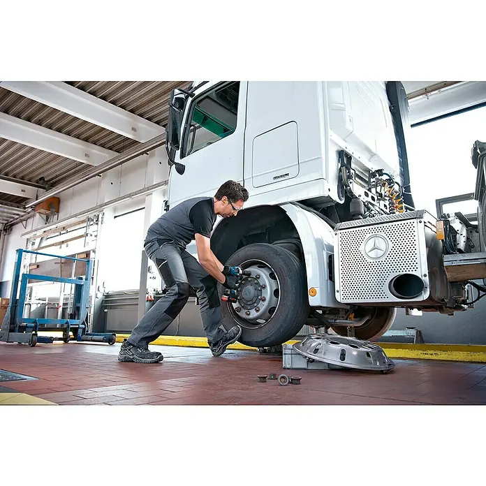 Bosch Professional AMPShare 18V Akku-Drehschlagschrauber - 18 V, 2 Akkus, 5,5 Ah, 1.000 Nm - Ein Mechaniker verwendet einen blauen und schwarzen Akku-Schlagschrauber, um an einem großen LKW-Reifen in einer Werkstatt zu arbeiten.