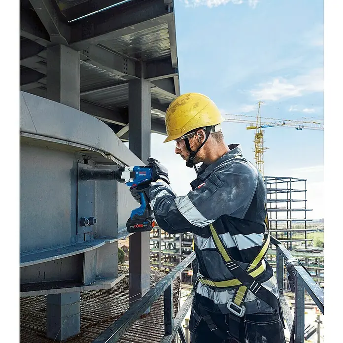 Bosch Professional AMPShare 18V Akku-Drehschlagschrauber - 18 V, 2 Akkus, 5,5 Ah, 1.000 Nm - Arbeiter verwendet blauen Bosch ProCORE 18V Schlagschrauber mit rotem Akku, um eine große Schraube an einem Metallträger festzuziehen.
