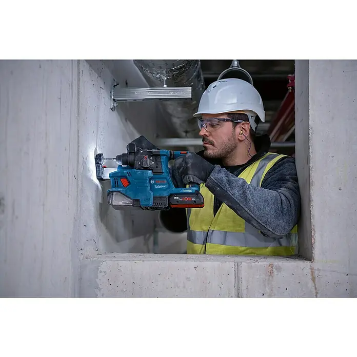 Bosch Professional AMPShare 18V Akku-Bohrhammer GBH 18V-22 GDE 18V-12 - 18 V, Ohne Akku, 1,9 J - Ein Arbeiter nutzt einen blauen Bosch Akku-Bohrhammer mit Staubabsaugung, um in eine Betonwand zu bohren.