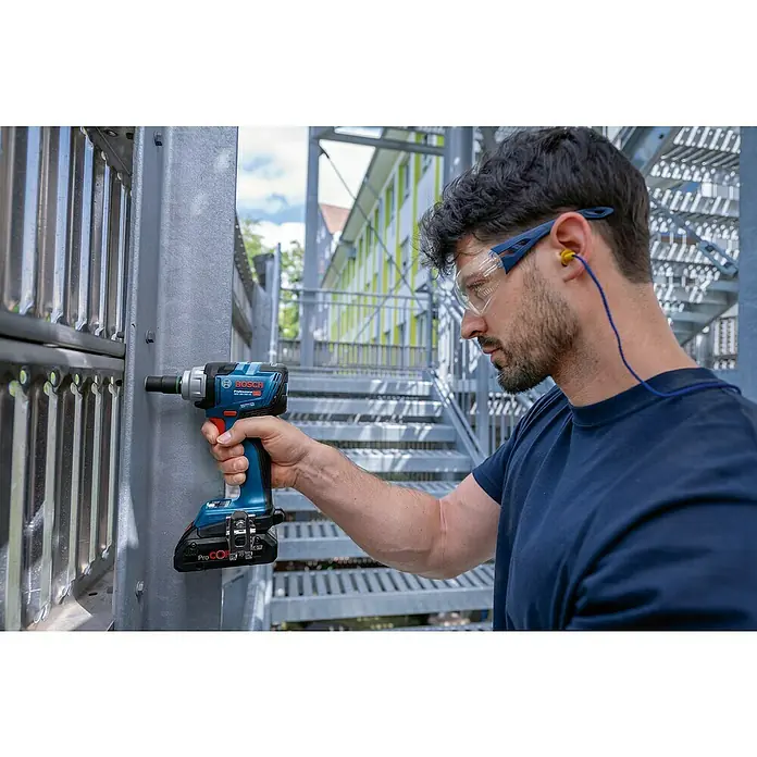Bosch Professional AMPShare 18V Akku-Drehschlagschrauber GDS 18V-330 HC - 18 V, 330 Nm, 1 x Bluetooth Low Energy Modul GCY 42 Professional, 2 x Akku ProCORE18V 4.0Ah - Mann in Schutzkleidung befestigt Bolzen an Metallkonstruktion mit blau-schwarzem Bosch Professional Akku-Schlagschrauber.