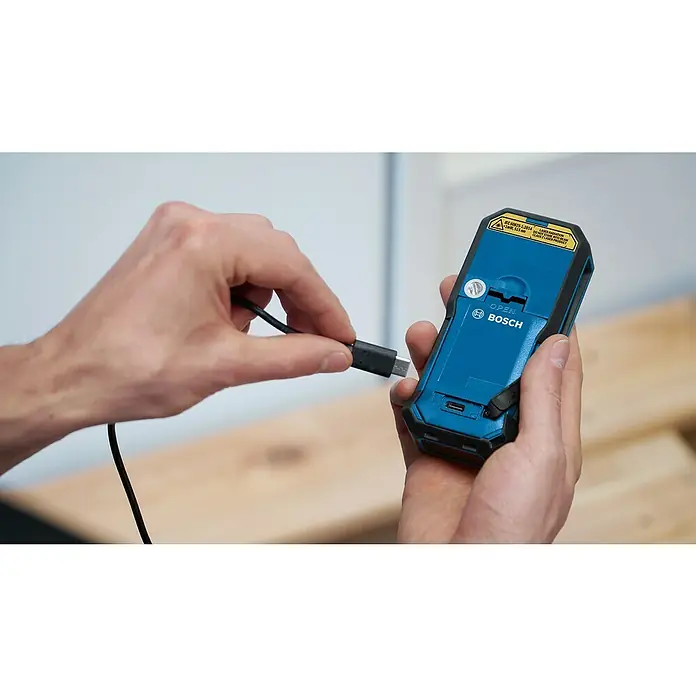 Bosch Professional USB-Akku-Adapter PRO BA 3.7V 1.0Ah A - Akkuspannung: 3,7 V, Höchste Leistung Einzelakku: 5 Wh - Hände stecken ein USB-C-Kabel zum Laden in ein blaues Bosch Laser-Messgerät.