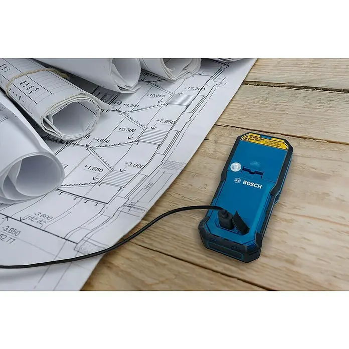 Bosch Professional USB-Akku-Adapter PRO BA 3.7V 1.0Ah A - Akkuspannung: 3,7 V, Höchste Leistung Einzelakku: 5 Wh - Blaues Bosch Laser-Messgerät mit schwarzem Kabel auf Bauplänen und Holzuntergrund.