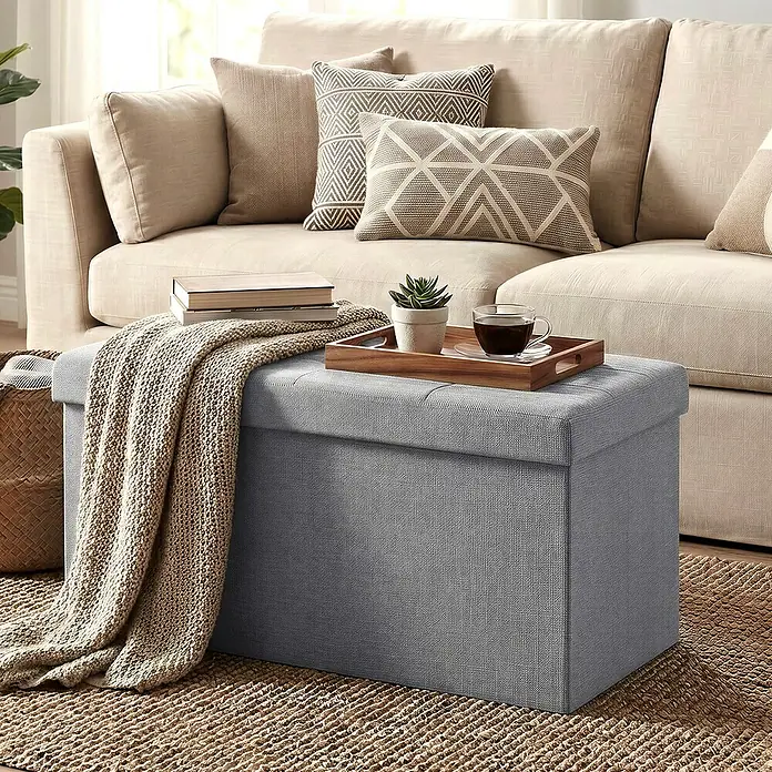 Hocker mit Stauraum - L x B x H: 38 x 76 x 38 cm, Hellgrau - Grauer Polsterhocker mit Stauraum neben einem beigen Sofa, darauf ein Tablett mit Kaffee und Pflanze, mit Strickdecke.