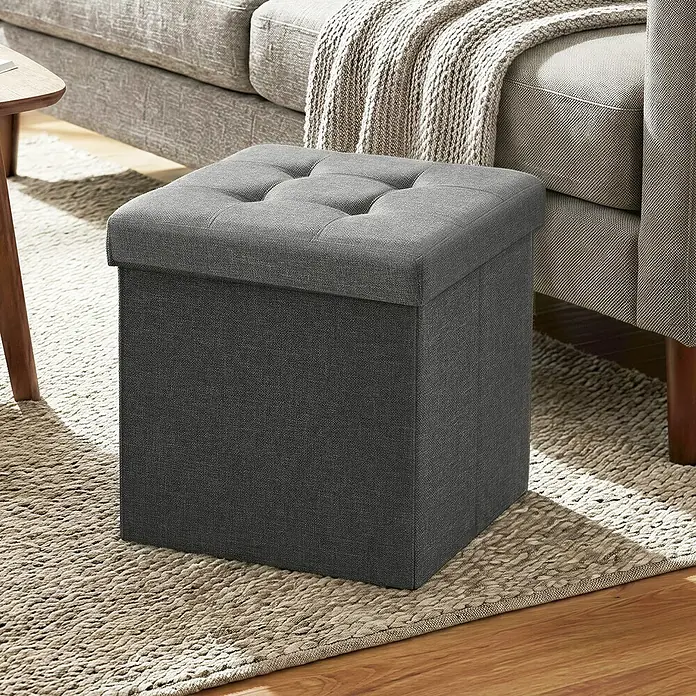 Hocker mit Stauraum - L x B x H: 30 x 30 x 30 cm, Grau - Dunkelgraue Stoff-Aufbewahrungsottomane mit getuftetem Deckel, auf einem Teppich neben einem Sofa.