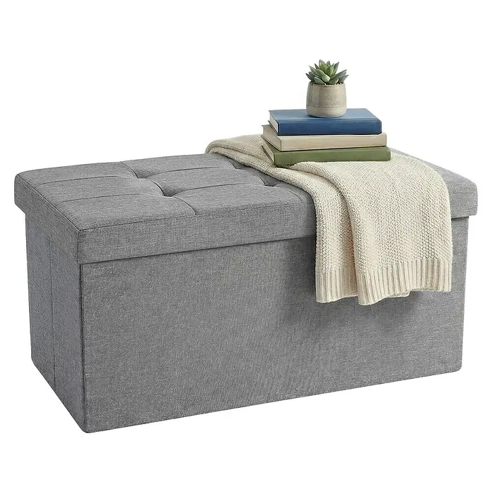 Hocker mit Stauraum - L x B x H: 38 x 76 x 38 cm, Hellgrau - Grauer Stoff-Aufbewahrungshocker mit getuftetem Deckel, dekoriert mit Decke, Büchern und Sukkulente.