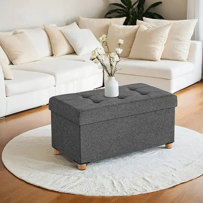 Hocker mit Stauraum - L x B x H: 38 x 76 x 40 cm, Grau - Dunkelgrauer getufteter Stauraum-Ottomane mit Holzbeinen auf einem weißen runden Teppich im Wohnzimmer.