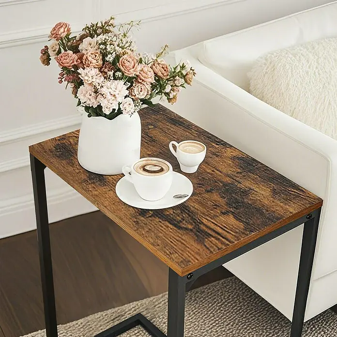 Beistelltisch - L x B x H: 35 x 55 x 55 cm, Schwarz/Braun - Rustikaler C-förmiger Beistelltisch mit Holzoptik-Platte und schwarzem Metallgestell, neben Sofa mit Blumen und Kaffeetassen.