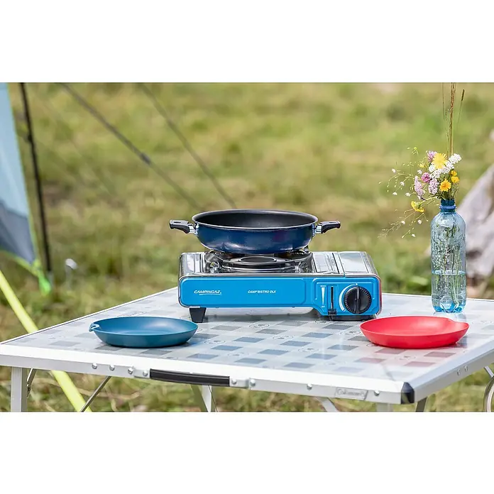 Campingaz Gaskocher Camp Bistro DLX - L x B x H: 285 x 370 x 125 mm, Leistung: 2.120 W, Ohne Stopgaz-System - Blauer und silberner Campingaz Camp Bistro DLX Gaskocher mit blauer Pfanne auf einem Campingtisch.