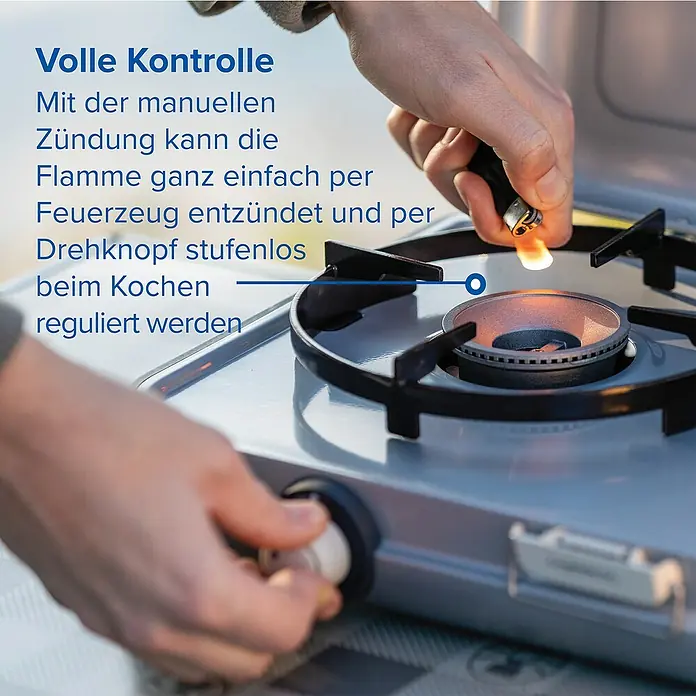 Campingaz Gaskochfeld Kitchen 2 - 2 Brenner, 2.000 W, L x B x H: 35 x 49 x 10 cm - Person zündet einen silbernen Gaskocher mit einem Feuerzeug und reguliert die Flamme mit einem Knopf.