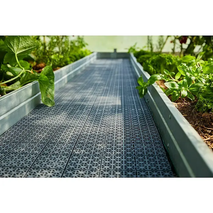 Loseta con sistema click - Polipropileno reciclado, 30 x 30 x 1,2 cm, Marrón, 1 ud. - Baldosas modulares de plástico gris con superficie estampada, formando un pasillo entre bancales elevados verdes.