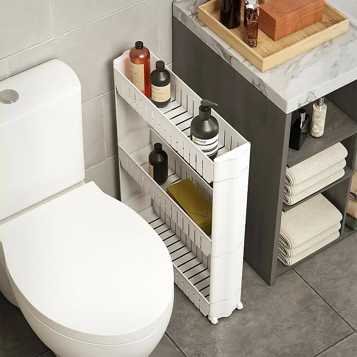 Versa Carro con ruedas multiusos de 3 baldas - L x An x Al: 54 x 12,5 x 71 cm, Termoplástico - Carro de almacenamiento blanco estrecho de varios niveles en un baño, encajando entre un inodoro y un tocador, con botellas y toallas.
