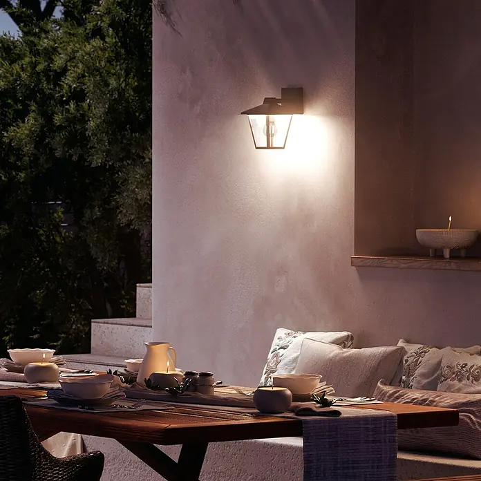 Philips Aplique exterior Kinno - 25 W, L x An x Al: 17 x 21 x 30 cm, Descendente - Aplique de pared exterior de metal oscuro con cristales, iluminando con luz cálida una mesa de comedor nocturna.