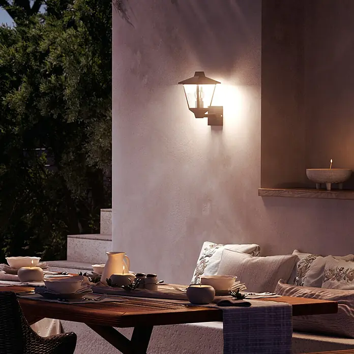 Philips Aplique exterior Kinno - 25 W, L x An x Al: 17 x 21 x 30 cm, Ascendente - Clásica lámpara de pared exterior negra ilumina una acogedora cena nocturna en un patio.